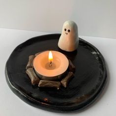 a lit candle sitting on top of a black plate next to a small white ghost