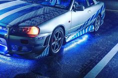 a silver car with blue stripes parked on the side of the road in the rain