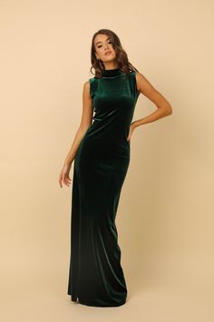 a woman wearing a green velvet dress with high neck and side slits, standing in front of a beige background