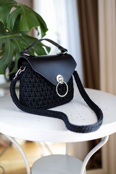 a black purse sitting on top of a white table next to a potted plant