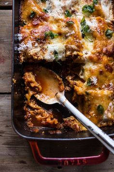 a casserole dish with meat, cheese and spinach is shown on a wooden table