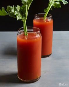 two glasses filled with tomato juice and garnished with parsley on the side