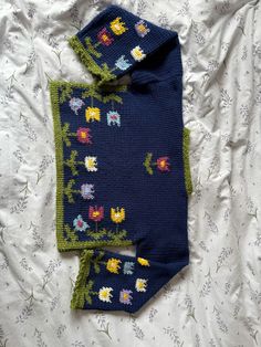 two pieces of knitted clothing laying on top of a white bed spread with flowers and leaves