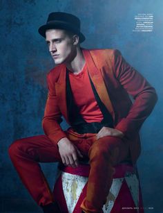 a man sitting on top of a red and white stool wearing a black fedora