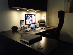 a desk with two monitors and a laptop on top of it in a dark room