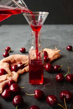 cherry juice being poured into a wine glass with cherries on the table next to it