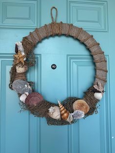 a wreath made out of burlocks and seashells hangs on a blue door