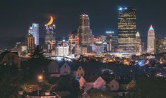 the city skyline is lit up at night, with buildings in the foreground and trees on the other side