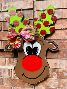 a reindeer head hanging on the side of a brick wall with red nose and green polka dots