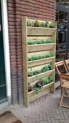 a wooden planter filled with plants next to a brick wall on the side of a building