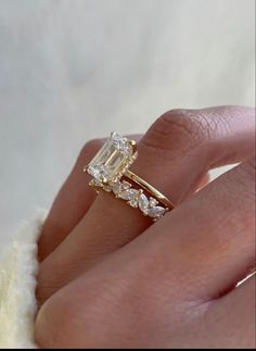 a woman's hand with a diamond ring on top of her finger and the other hand holding an engagement ring