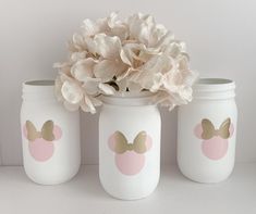 three white mason jars with pink and gold minnie mouse decals on them, one has a flower in it