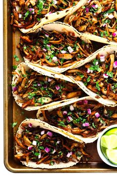 several tacos are lined up on a tray with limes and cilantro