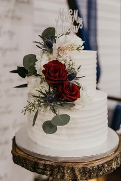 a white wedding cake with red roses and greenery