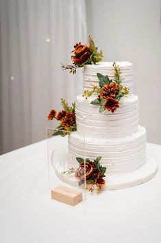 a white wedding cake with orange flowers on the top and bottom tier is sitting on a clear acrylic stand