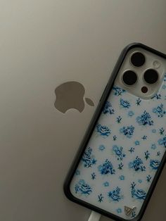 an iphone case with blue flowers on it sitting next to the back of an apple phone