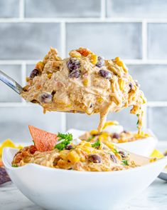 a spoon full of mexican dip being lifted from a bowl with tortilla chips