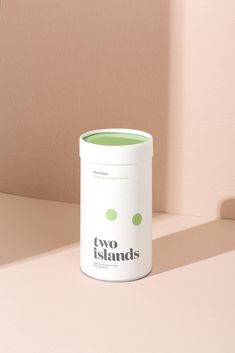 a white can sitting on top of a table next to a light pink wall with the words two islands printed on it