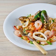 a white plate topped with pasta and shrimp on top of a wooden table next to a fork