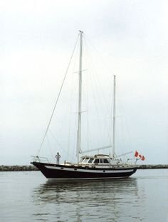 a sailboat in the water with two people standing on it's front end