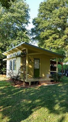 a small yellow house sitting on top of a lush green field next to a forest