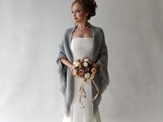 a woman in a white dress and gray cardigan is holding a bouquet of flowers