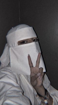 a person wearing a white mask making the peace sign