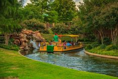 a boat filled with people riding down a river next to a lush green park area