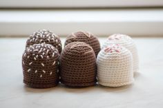 four crocheted baby hats sitting on top of a white table next to a window