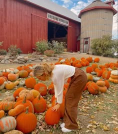 a woman picking up pumpkins in front of a barn