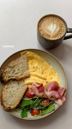 an omelet with bacon, lettuce and tomatoes on a plate next to a cup of coffee