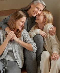 an older woman and two younger women sitting on the floor hugging each other with their arms around one another