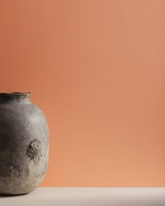 a black vase sitting on top of a white table next to an orange wall with a plant growing out of it