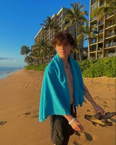 a man standing on top of a sandy beach next to the ocean with a blue towel over his shoulders