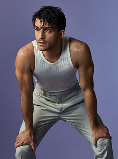 a man with his hands on his hips posing for a photo in front of a purple background