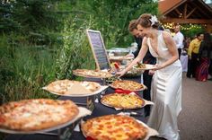 a woman standing in front of a table filled with lots of pizzas and pies