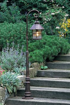 a lamp post sitting on the side of some steps in front of bushes and flowers