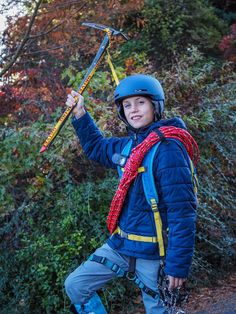 a young boy in blue jacket and helmet holding up a large pair of skis