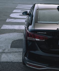 the back end of a black car parked in a parking lot next to an intersection