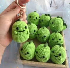 a person holding a small green crocheted keychain in front of a bunch of little balls