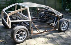 a car made out of wood sitting on top of a brick road next to a building