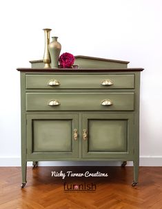 a green dresser with two vases on top and one red flower in the middle