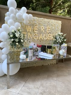 a table with balloons and flowers on it in front of a sign that says we are engaged