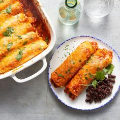 an enchilada and black beans are on a plate next to a casserole dish