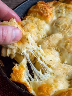 a hand holding a piece of bread with cheese on it in a skillet,