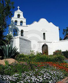 an old white church surrounded by flowers and greenery on a sunny day in california