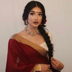 a woman wearing a red and gold sari with her hair in a fishtail braid