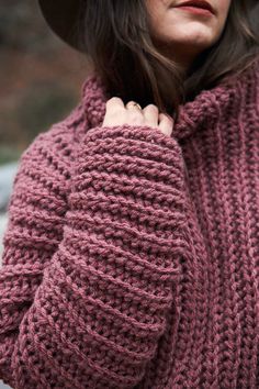 a woman in a hat and sweater is holding her hand on her shoulder while looking off to the side