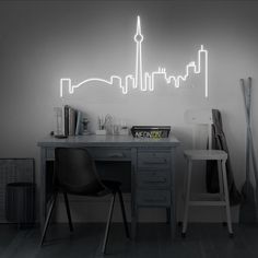 a black and white photo of a desk with a neon city skyline on the wall