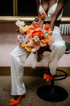 a woman is sitting on a stool with flowers in her lap and orange high heels